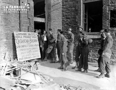 Des civils et des soldats américains font la queue à l'entrée d'un théâtre improvisé près de décombres. A l'affiche :"Casanova Brown" avec Gary Cooper et Theresa Wright.